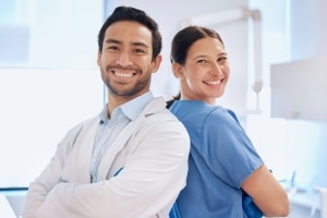 Two medical professionals smiling back to back with their arms crossed